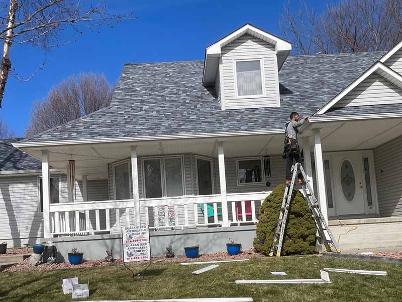 Guaranteed Affordable Roofing worker on a ladder inspecting the roof they just finished installing new gray shingles for